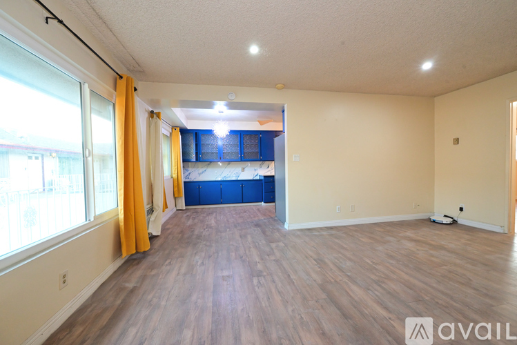 A spacious room with wooden flooring and a large window with yellow curtains.