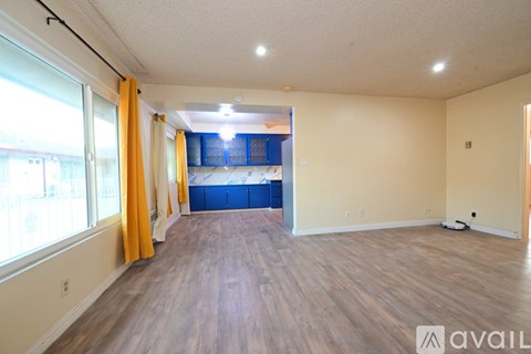 A spacious room with wooden flooring and a large window with yellow curtains.