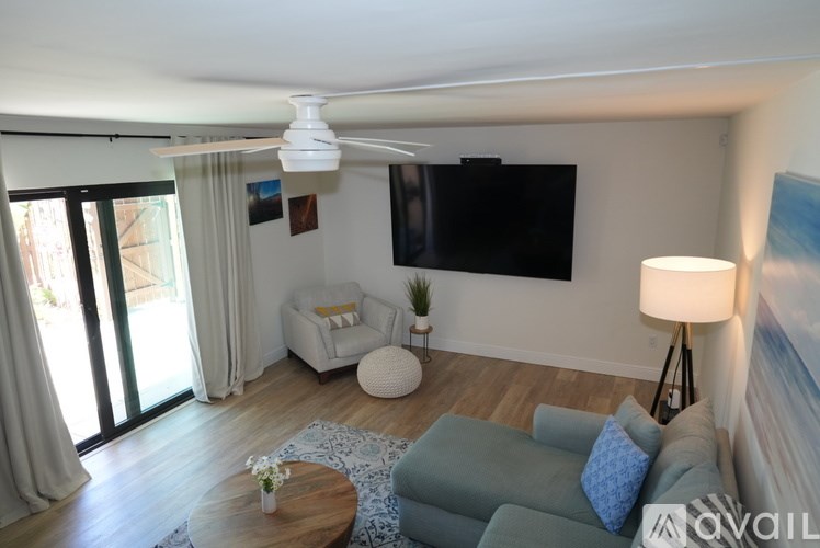 A living room with a grey couch, a white side table, a wooden coffee table, a flat screen TV, and a sliding glass door.