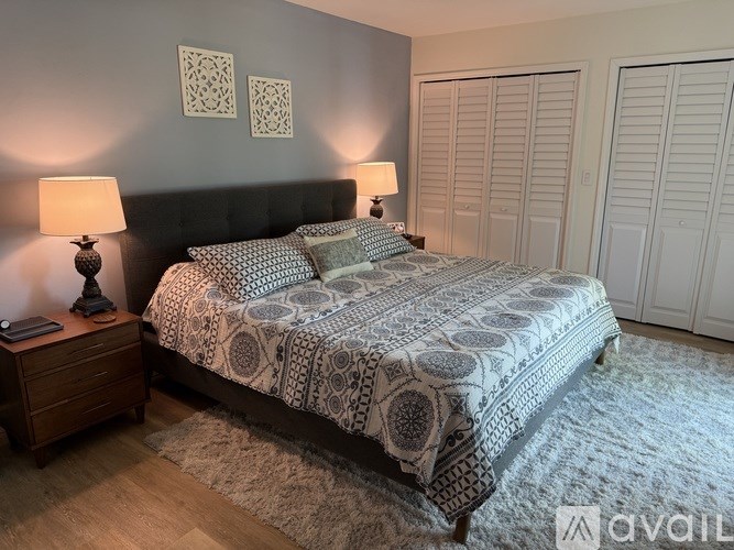 A bed with a patterned comforter and two pillows sits in a room with a wooden nightstand and two lamps.