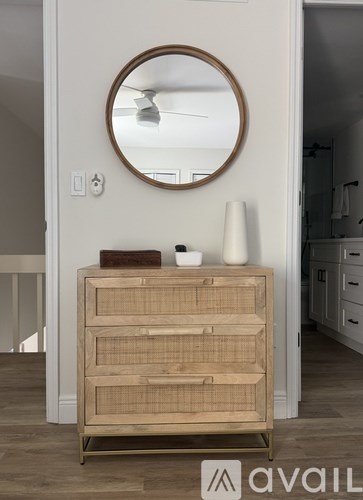 A wooden chest of drawers with a round mirror above it.