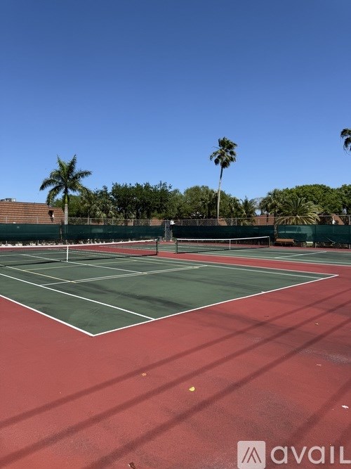 A tennis court with a green and red surface surrounded by a fence and palm trees.