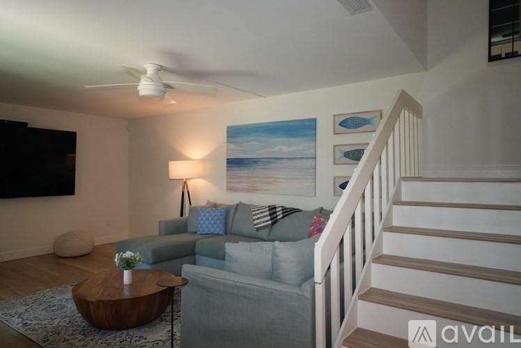 A living room with a grey couch, a wooden coffee table, a staircase, and a painting on the wall.