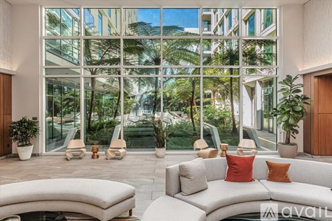 A living room with a white couch and a large window with a view of trees.
