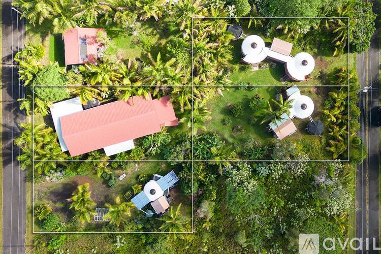 A bird's eye view of a lush green area with a red building and a white circular structure.