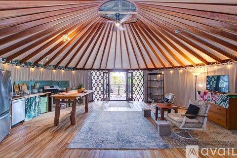 The image shows a cozy interior of a yurt with a wooden floor, a table with chairs, and a kitchen area.