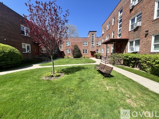 A tree with red leaves is in the middle of a grassy area in front of a brick building.