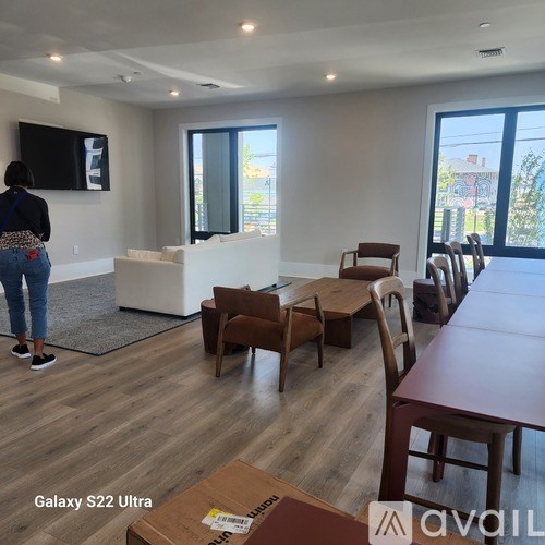 A woman is standing in a room with a TV mounted on the wall and a table with chairs.