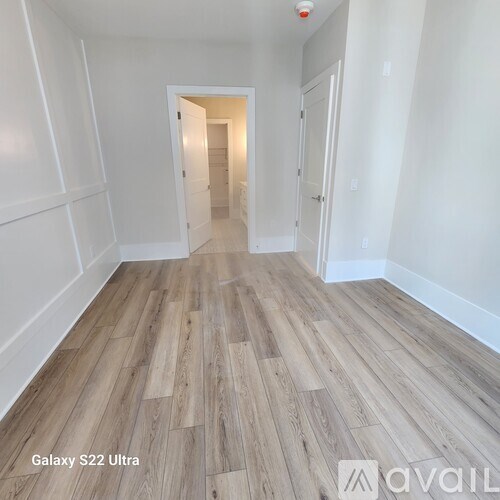 A room with wooden flooring and white walls, with a doorway leading to another room.