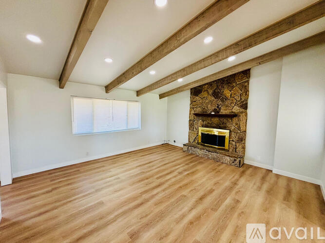 A spacious room with wooden floors and a stone fireplace.