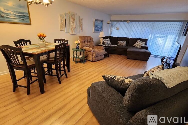 A living room with a brown couch, a dining table with chairs, and a small ottoman.