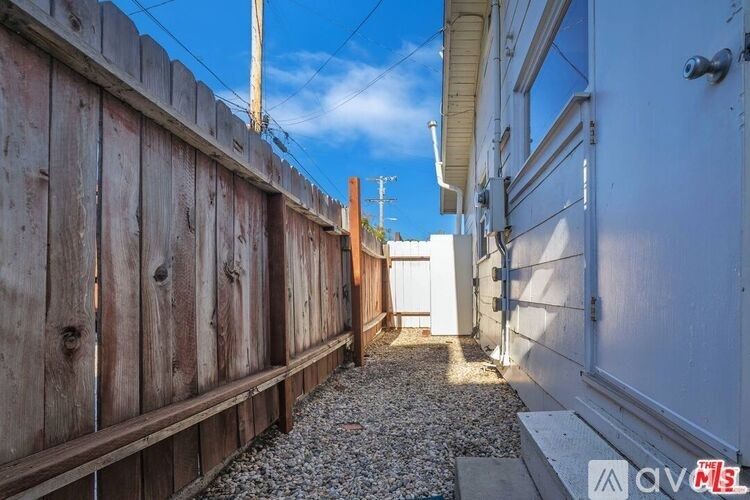 A narrow alley with a wooden fence on the left and a white building on the right.