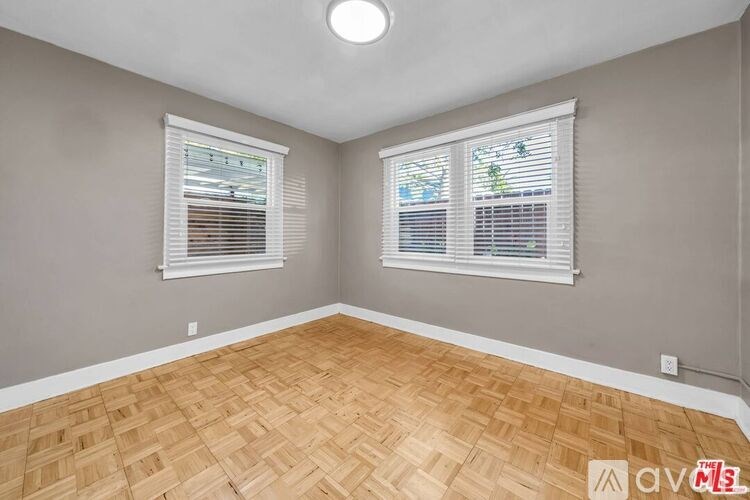 A room with wooden flooring and two windows with blinds.