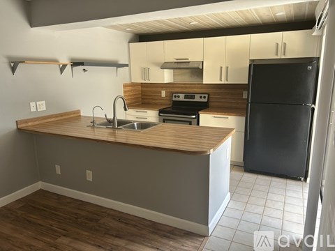 A kitchen with a black refrigerator and wooden countertops.