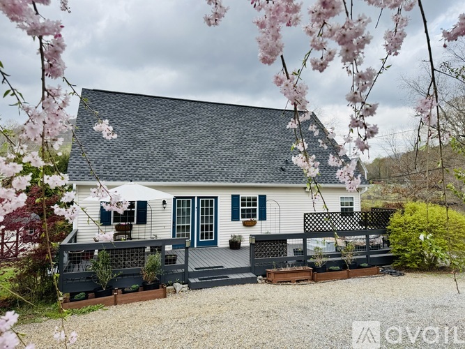 A house with a grey roof and white walls is surrounded by a gravel driveway and a fence.