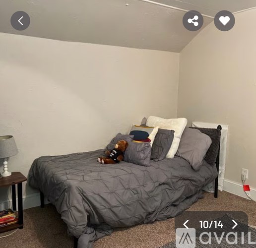 A bedroom with a bed covered in a grey comforter and a teddy bear on the pillow.