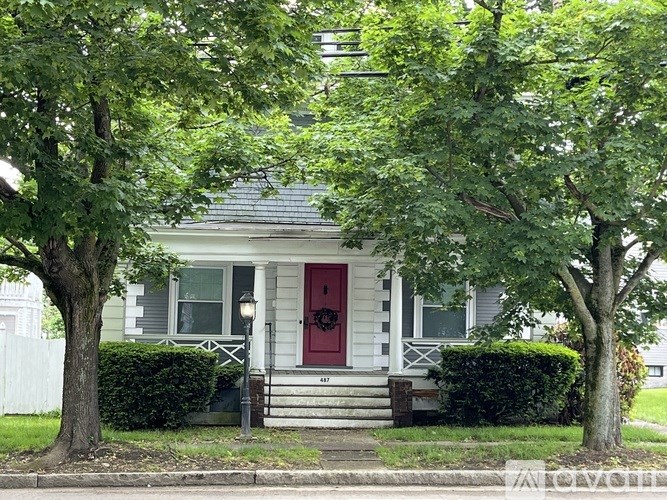 A house with a red door is surrounded by green trees.