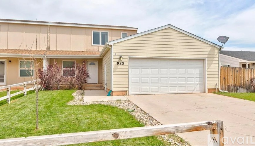 A beige house with a white garage door and a small tree in front.