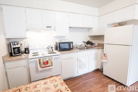 A kitchen with white cabinets and appliances, a refrigerator, and a rug on the floor.