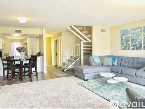 A living room with a grey couch and a dining table with chairs.