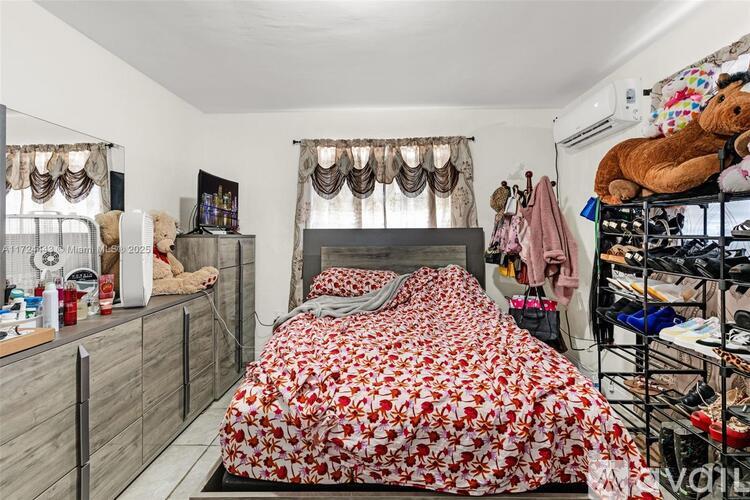 A bedroom with a bed covered in a red and white floral bedspread, a wooden dresser, and a shelf with various items.