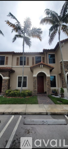 A house with a brown door and windows is surrounded by palm trees.