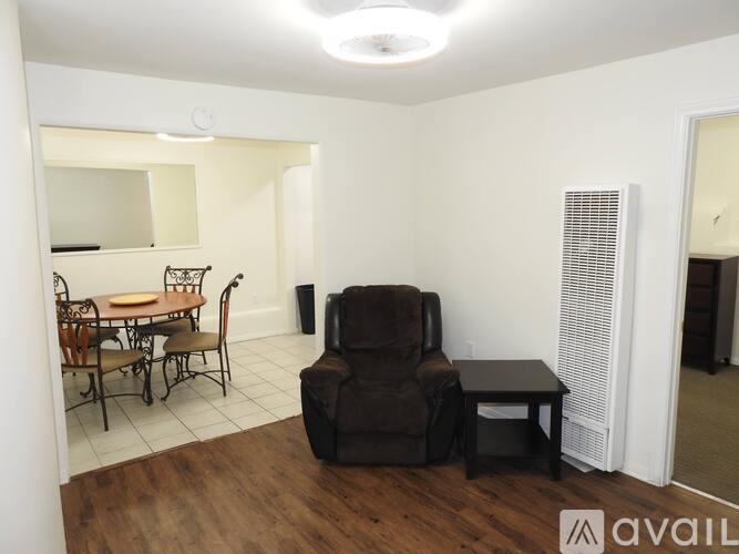 A living room with a brown recliner, a small table, and a dining table with chairs.