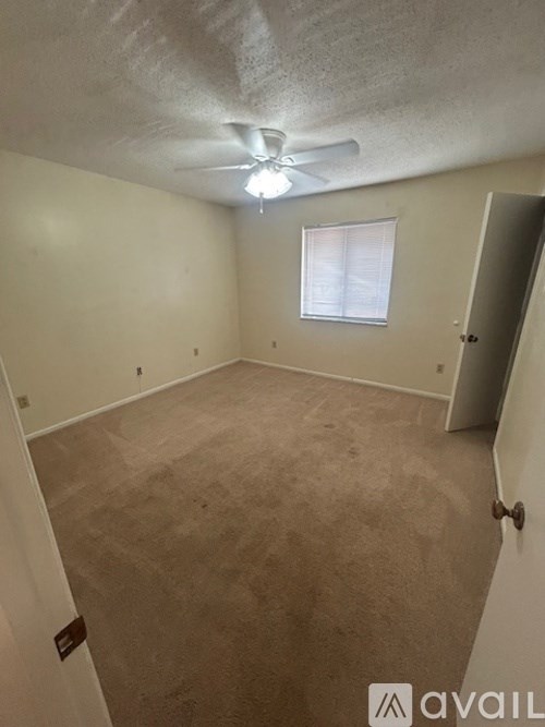 A room with a carpeted floor, a ceiling fan, and a window with blinds.