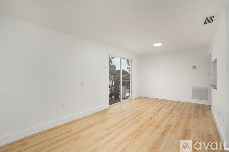 A spacious room with wooden flooring and a sliding glass door leading to a balcony.
