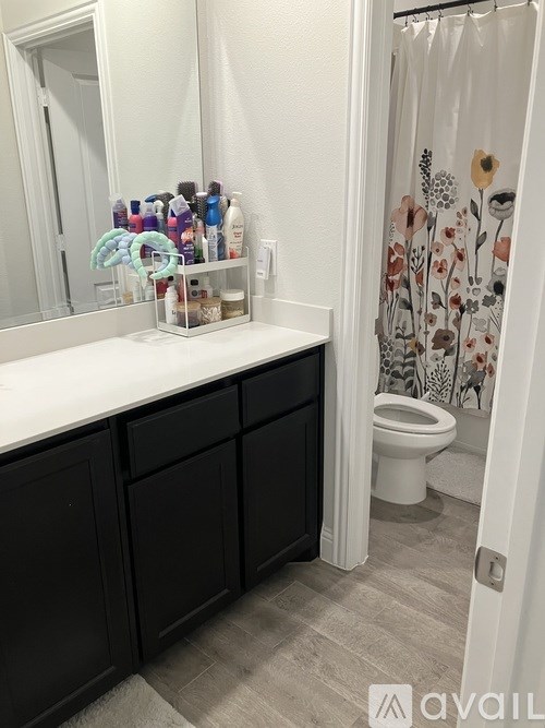 A bathroom with a white countertop, black cabinets, and a shower with a floral curtain.