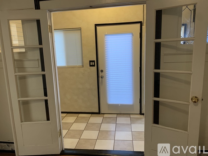 A white door with a black handle is open to a room with a white door and a window with blinds.