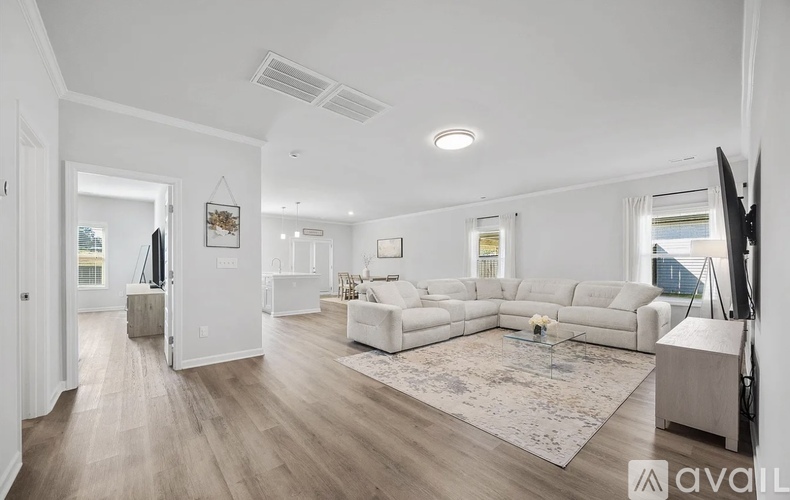 A spacious living room with a white sofa set and a rug in the center.