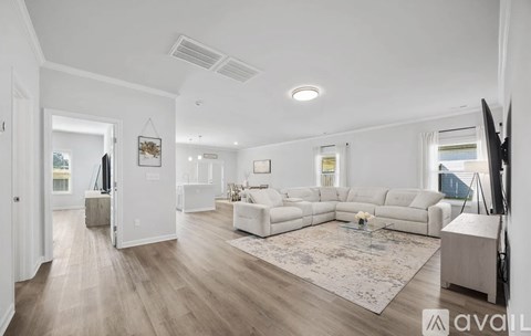 A spacious living room with a white sofa set and a rug in the center.