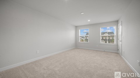 A room with beige carpet and two windows showing a view of buildings outside.