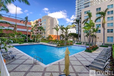 A pool surrounded by lounge chairs and umbrellas with a building in the background.
