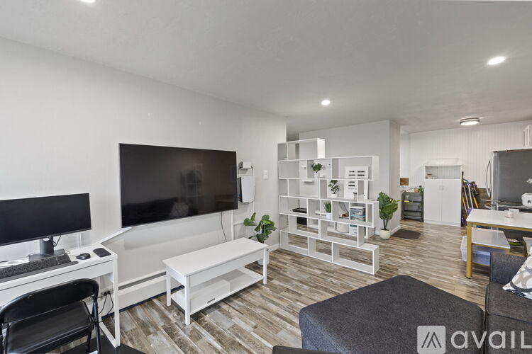 A modern living room with a white sofa, a black chair, a TV, and a wooden floor.