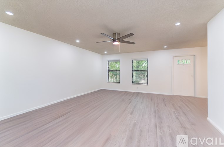A spacious room with a ceiling fan and two windows.