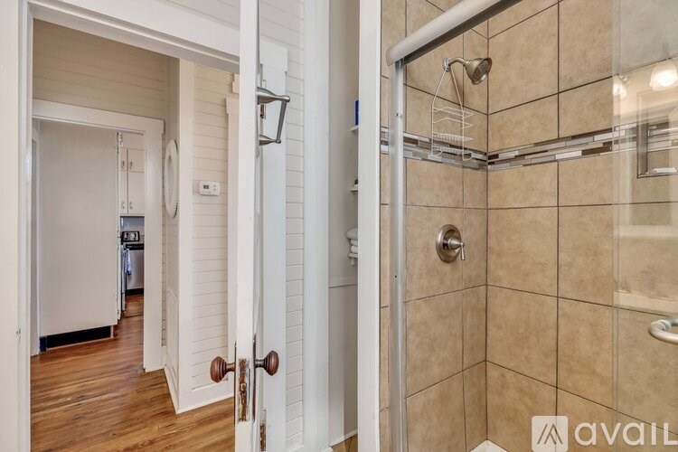 A bathroom with a walk-in shower and a doorway leading to a kitchen.