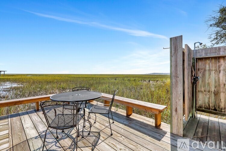 A wooden deck with a table and chairs overlooking a marsh.