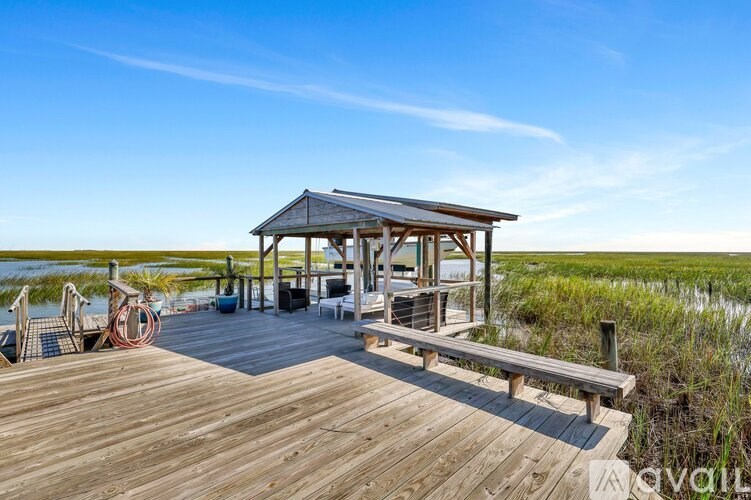A wooden deck with a gazebo and chairs overlooking a marshy area.