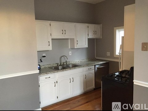 A kitchen with white cabinets and a black trash bin.