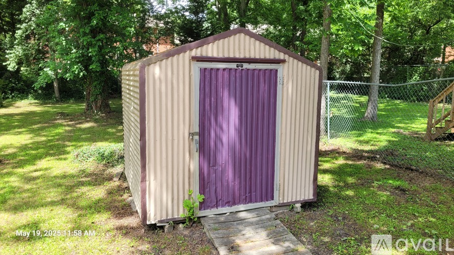 A shed with a purple door is situated in a grassy area.