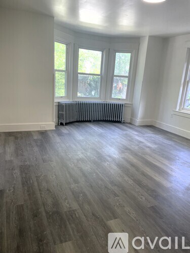 A room with wooden flooring and a window with a radiator beneath it.
