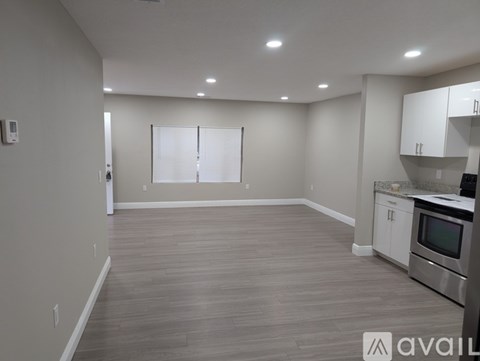 A spacious kitchen and living room with wooden flooring and white cabinetry.