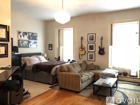 A living room with a couch, a bed, and guitars on the wall.