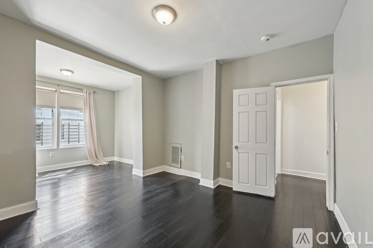 A spacious room with wooden floors and a large window with curtains.