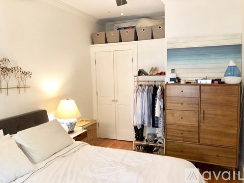 A bedroom with a bed, a nightstand with a lamp, a wardrobe, and a wooden dresser.