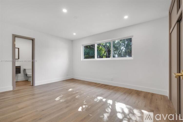 A room with wooden flooring and a window showing trees outside.