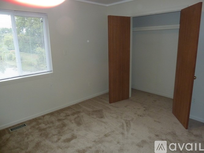 A room with a carpeted floor, a window with blinds, and a door with a wooden frame.