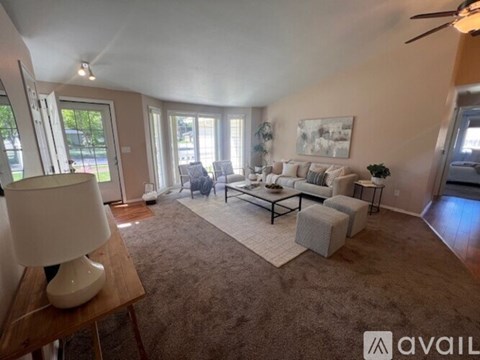 A living room with a grey carpet and a white lamp on a wooden table.